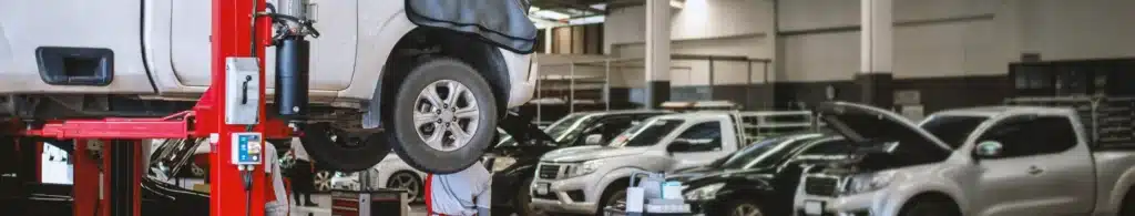 Auto repair near me in Olyphant, PA with Olyphant Auto Services. Image of mechanic performing auto repair on a truck lifted in the shop bays with other trucks and cars with hoods up in the background.