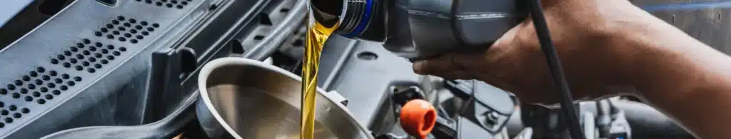 Oil change services in Olyphant, PA with Olyphant Auto Services. Image of mechanic pouring new oil into a car engine that came in the shop for an oil change.